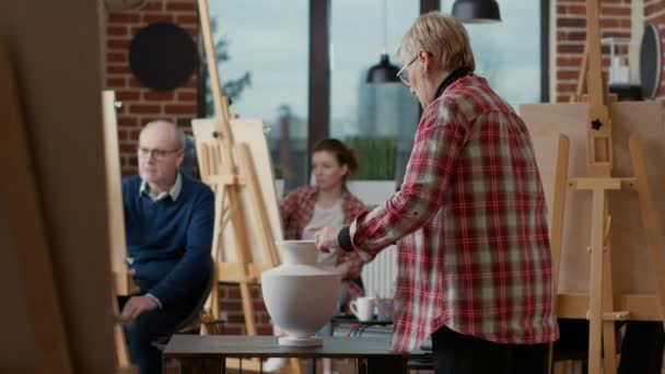 Äldre konstnär pekar på vas på bordet för att förklara teckningsteknik — Stockvideo