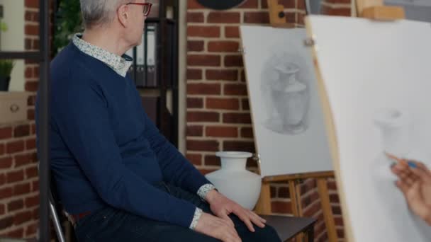 Старший художник, який демонструє модель вази людям, які відвідують практику семінару — стокове відео