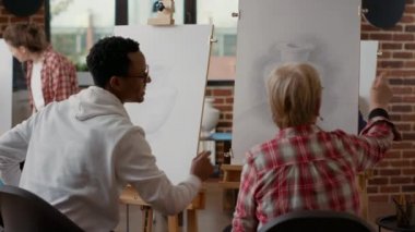 Afrikalı Amerikalı bir adam sanat sınıfında son sınıf öğrencisine yardım ediyor.