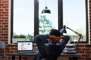 Yorgun bir başlangıç sahibi maske takıyor ve dizüstü bilgisayarın önünde oturuyor.