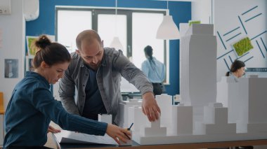 Kadın ve erkek şehir inşaatının planlarını ve modelini analiz ediyor.