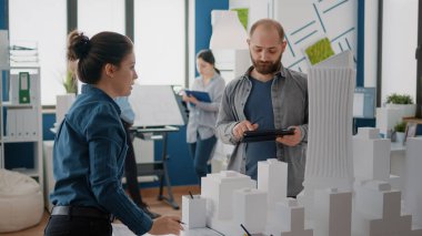 Erkek ve kadın dijital tablet ve inşa modeli ile inşaat planı planlamak için takım çalışması yapıyorlar.