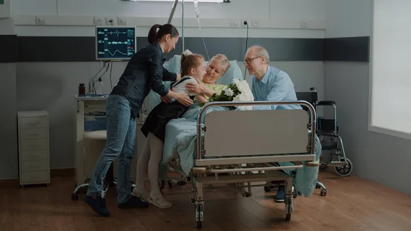 Child surprising ill woman with bouquet of flowers in hospital ward — Stock Photo, Image
