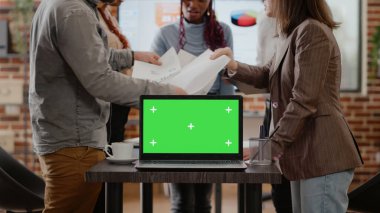 Çalışma arkadaşlarının masasında yeşil ekranlı dizüstü bilgisayarı var.