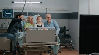 Family watching television and visiting senior patient in hospital ward