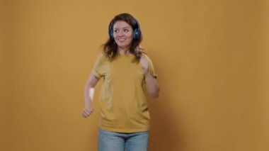 Kablosuz kulaklıkla iyimser müzik dinleyen ve stüdyoda tuhaf dans hareketleri yapan sıradan bir kadının portresi. Enerjik, kulaklıklı, parti veren ve yalnız dans eden pozitif bir kadın..