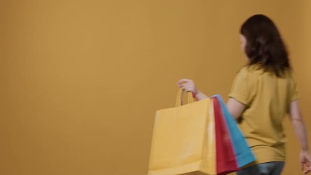 女性为在工作室购买产品而感到自豪的画像 微笑着拿着购物袋的人 对黄色背景的询问感到欣喜若狂 — 图库视频影像