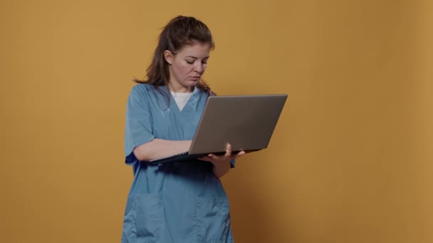 忙碌的医生站在那里 拿着笔记本电脑 在键盘上打字 在工作室里看着屏幕的画像 医院制服医疗人员使用手提电脑作医疗概念作广告宣传 — 图库视频影像