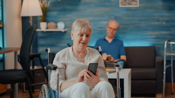 Oudere die in een rolstoel zit en een smartphone gebruikt — Stockfoto