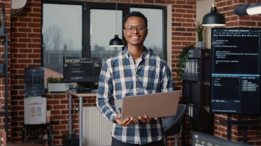 Afro-Amerikan programcının portresi dizüstü bilgisayarda çalışıyor ve gülümsüyor.