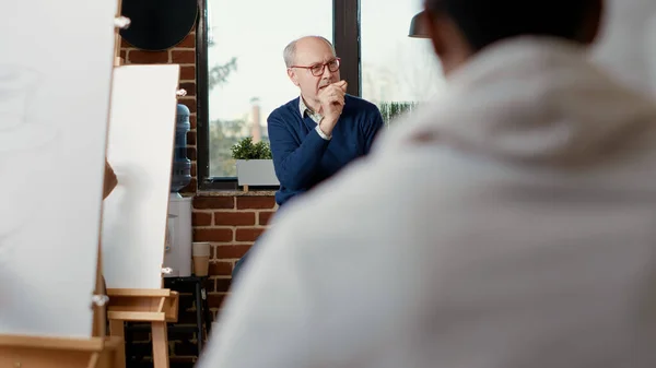 Starší muž učí studenty umění kreslit kresby na plátno — Stock fotografie