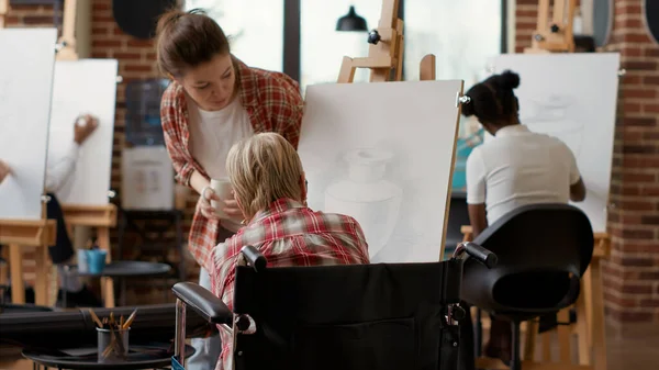 Старший по возрасту человек в инвалидной коляске рисует модель вдохновения в художественном классе — стоковое фото