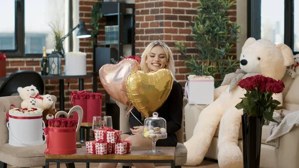 Souriant belle femme le jour de la Saint-Valentin tenant ballons en forme de coeur d'hélium dans la chambre pleine de cadeaux de luxe — Photo