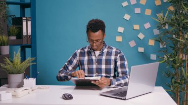 Belgeler ve dizüstü bilgisayarlardaki iş çizelgelerini analiz eden genç bir çalışan.