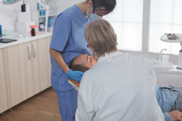 患者の口を調べる顔マスクを持つ臨床歯科矯正医チーム — ストック写真