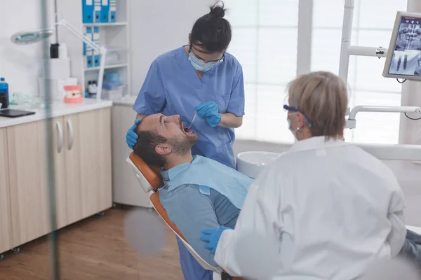 Specjalistyczna pielęgniarka nosząca maskę twarzy podczas analizy zębów pacjenta — Zdjęcie stockowe