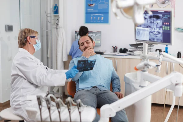 歯の放射線撮影を説明顔マスクを持つシニア歯科医の女性 — ストック写真