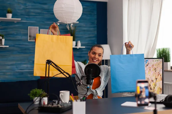 Criador de conteúdo de mulher mostrando sacos de papel coloridos para doação online. — Fotografia de Stock
