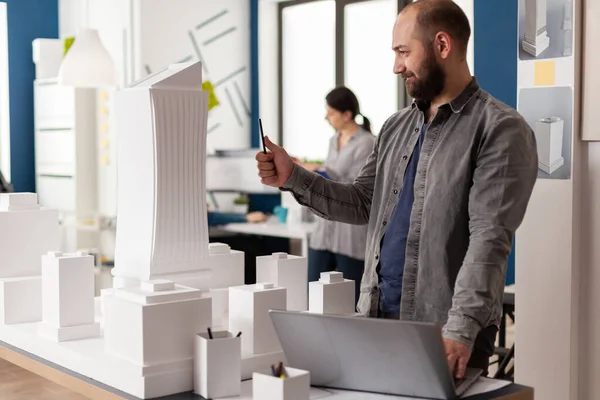 Inspirerad arkitekt med bärbar dator tittar på de arkitektoniska linjer av vitt skum modell av bostadsprojekt — Stockfoto