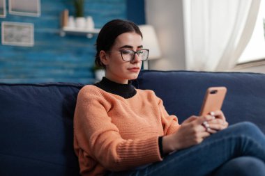 Öğrenci kanepede dinleniyor. Akıllı telefonu tutuyor ve ekrana bakıyor..