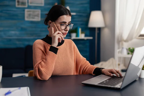 Estudante em casa falando ao telefone enquanto usa laptop. — Fotografia de Stock