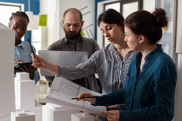 Dos mujeres ingenieros de arquitectura mirando hacia abajo en los planos junto a los colegas que sostienen el ordenador portátil — Foto de Stock