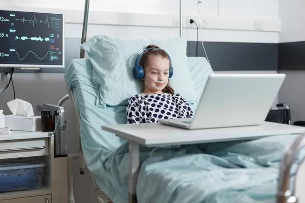 Молодая пациентка сидит в детской больничной койке и смотрит смешные мультики. — стоковое фото
