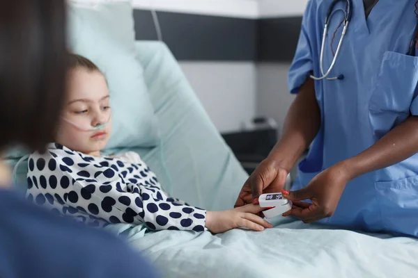 Enfermera de clínica pediátrica midiendo niveles de oxígeno de niña enferma usando oxímetro. — Foto de Stock