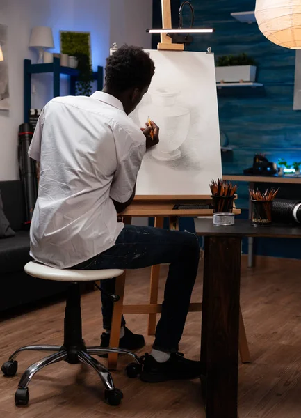Junger Mann sitzt vor Leinwand und skizziert Vase — Stockfoto