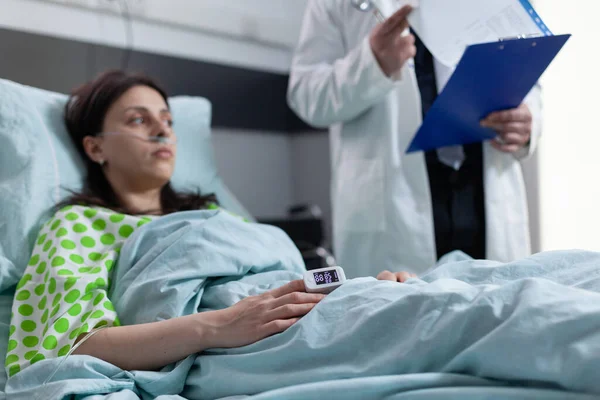 Mulher na cama do hospital com oxímetro de pulso no dedo mostrando baixa saturação de oxigênio ouvindo o médico — Fotografia de Stock