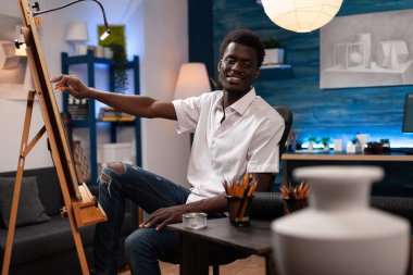 Afrikalı Amerikalı ressam tuvalin önünde oturmuş vazo çiziyor.