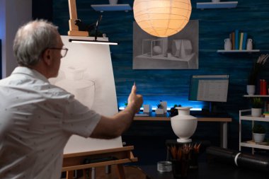 Kıdemli ressam, palmiye vazosuna bakarken, ölçeklendirmek için sivri kalem kullanarak ilham aldığını düşünüyor.