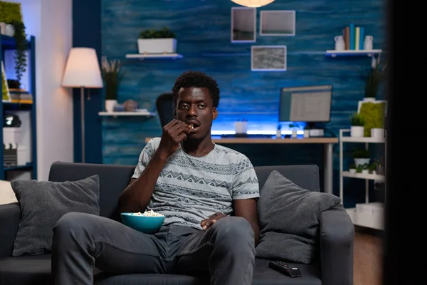 Alone guy sitting on sofa holding bowl with popcorn eating