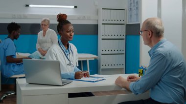 Doktor muayenehanesinde hasta olan yaşlı bir hastaya danışıyor.