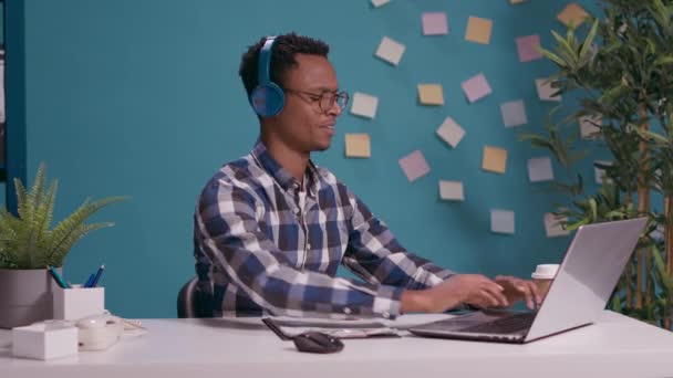 Работник офиса слушает музыку и поет, пользуясь ноутбуком — стоковое видео