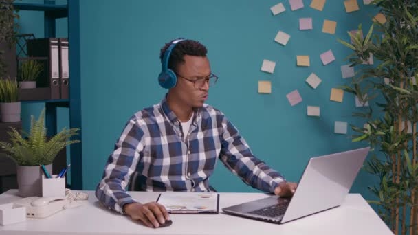 在办公桌前的笔记本电脑上工作和听音乐的现代人 — 图库视频影像