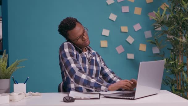 Pracownik biurowy rozmawia przez telefon i używa laptopa do pracy — Wideo stockowe