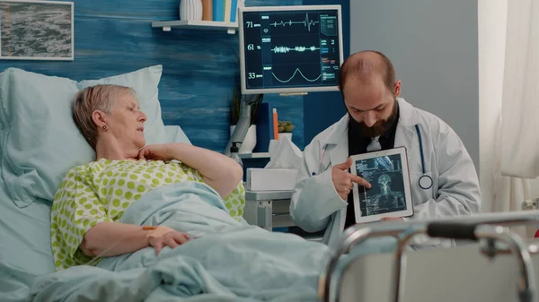 Læge, der viser osteopati x ray på tablet til ældre kvinde - Stock-foto