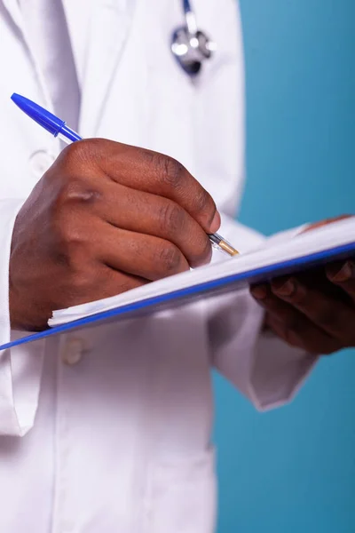 Primer plano de la mano del médico afroamericano sosteniendo bolígrafo escrito en el portapapeles —  Fotos de Stock