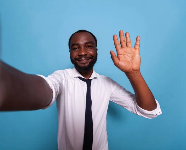 Улыбающийся видеоблогер машет приветствием перед камерой на видеоконференции — стоковое фото