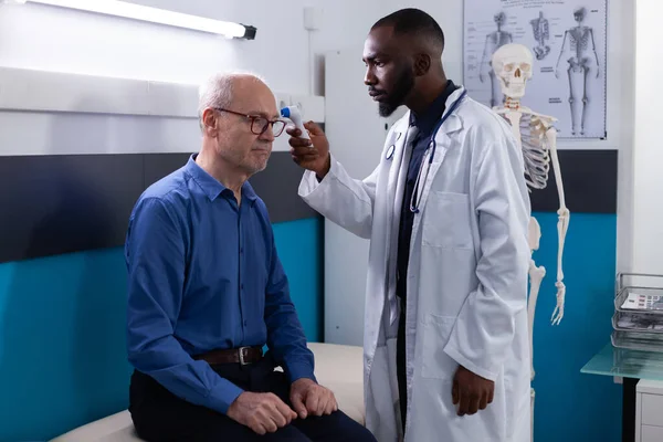 Médico afroamericano que pone termómetro infrarrojo en la frente de un paciente mayor —  Fotos de Stock