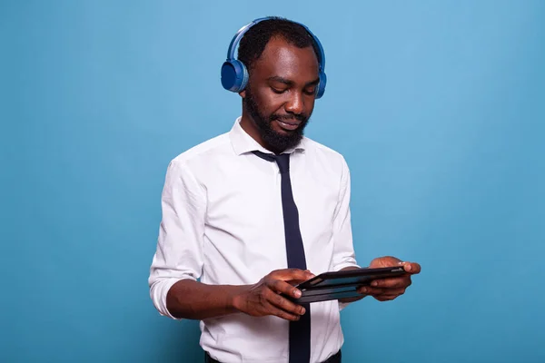 Hombre de camisa blanca relajándose con auriculares inalámbricos mirando el espectáculo en línea en la computadora tableta —  Fotos de Stock
