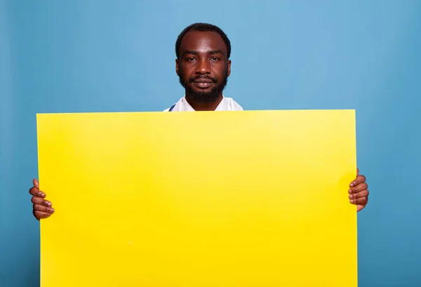 Médecin souriant tenant grand carton vide jaune pour les soins de santé concept médical — Photo