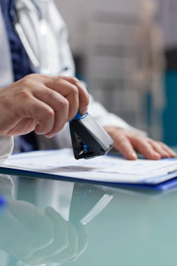 Doktorun elinde reçeteye yazılacak tıbbi bir pul var.