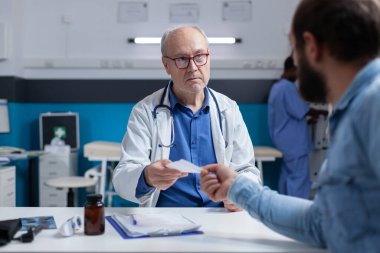 Sağlık kontrolünde doktor hasta olan hastaya reçeteli dosya veriyor.