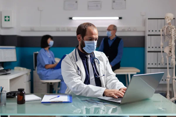 Allmänpraktiserande läkare med vit rock som arbetar på laptop på läkarmottagningen — Stockfoto