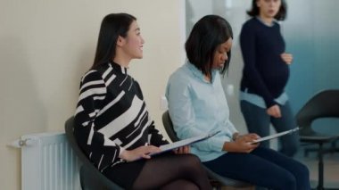 Asyalı ve Afrikalı Amerikalı kadınlar iş görüşmesinde bekleme salonunda konuşuyorlar.