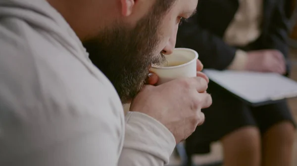 Primo piano dell'uomo che beve una tazza di caffè e trema alla sessione di terapia di gruppo aa — Foto Stock