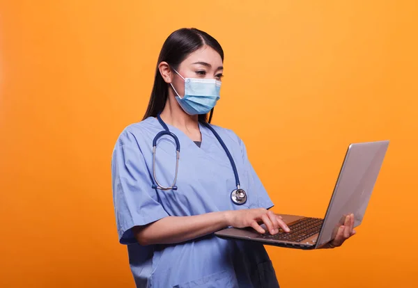 랩탑을 사용하는 동안 바이러스 보호용 면도기와 청진기를 착용하는 젊은 성인 간호사. — 스톡 사진