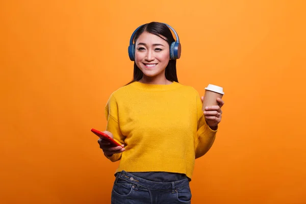 Bela feliz positivo ásia mulher vestindo moderno sem fio fones de ouvido enquanto tendo um xícara de café. — Fotografia de Stock